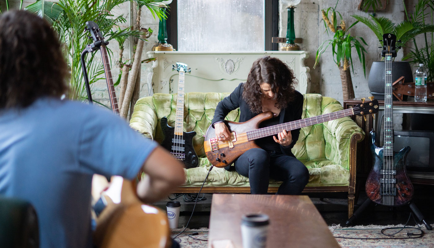 Woman playing a Spector bass on a vintage green sofa